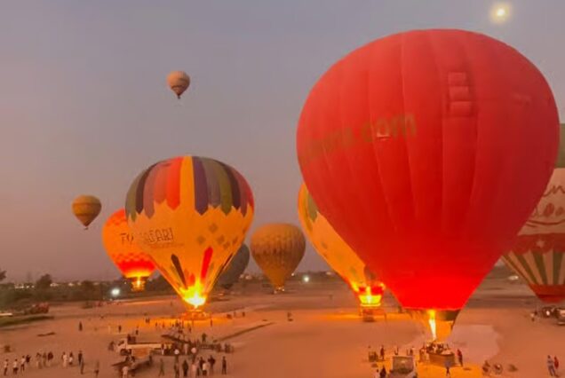 Multiple hot air balloons prepare for or take flight at sunrise, offering panoramic views of the landscape, likely in Luxor, Egypt.