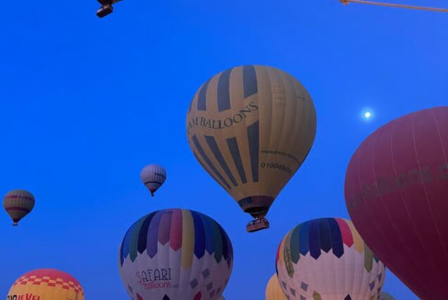 Hot air balloons rise at sunrise over Luxor, Egypt, with views of temples, the Nile River, and desert landscapes.