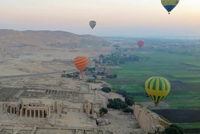 Hot air balloons floating over the West Bank of Luxor at sunrise, with views of the Nile River valley and ancient temples.