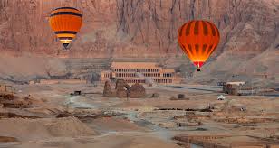 "Hot air balloons flying over Luxor, Egypt, with the Temple of Hatshepsut visible on the West Bank."