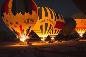 "Hot air balloons being inflated for a sunrise flight in Luxor, Egypt, with burners glowing in the early morning light."