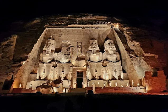 The Great Temple of Abu Simbel illuminated at night with spotlights highlighting the colossal statues of Ramesses II.