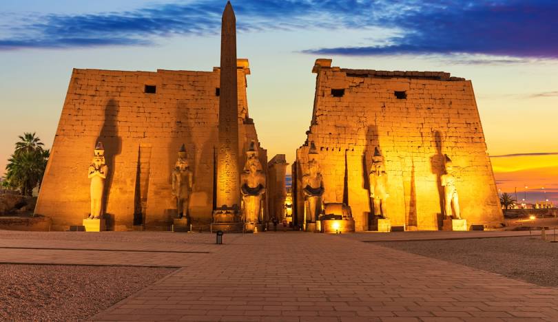 Luxor Temple illuminated at dusk in Luxor, Egypt, showcasing its pylon, statues, and ancient architecture.