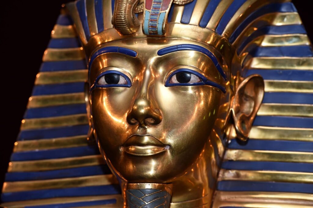 "Golden funerary mask of Pharaoh Tutankhamun, featuring a blue-striped nemes headdress, uraeus cobra, vulture, and false beard, displayed at the Egyptian Museum in Cairo."