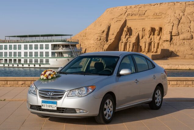 Hyundai Elantra wedding car with floral decoration parked near the Nile in Aswan, with a cruise ship and Abu Simbel temples in the background.