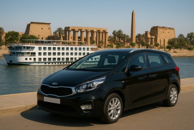 A black Kia Carens parked along the Nile River in Luxor, Egypt, with Luxor Temple and a Nile cruise ship in the background.