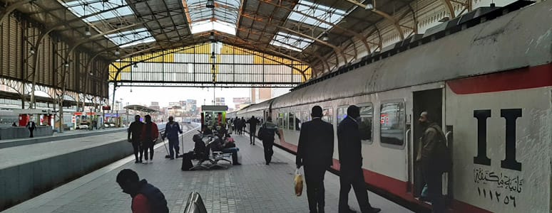Platform scene at an Egyptian National Railways (ENR) station with a second-class air-conditioned carriage marked "ثانية مكيفة" and passengers waiting or boarding.