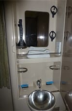 Washbasin area inside a cabin on an Egyptian sleeper train, featuring a metal basin, mirror, shelves, towel racks, and control knobs.