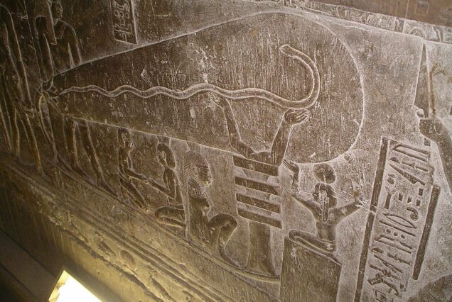 Relief carving at the Temple of Hathor in Dendera, Egypt, known as the “Dendera Light,” depicting a djed pillar supporting an oval container with a snake emerging from a lotus flower.