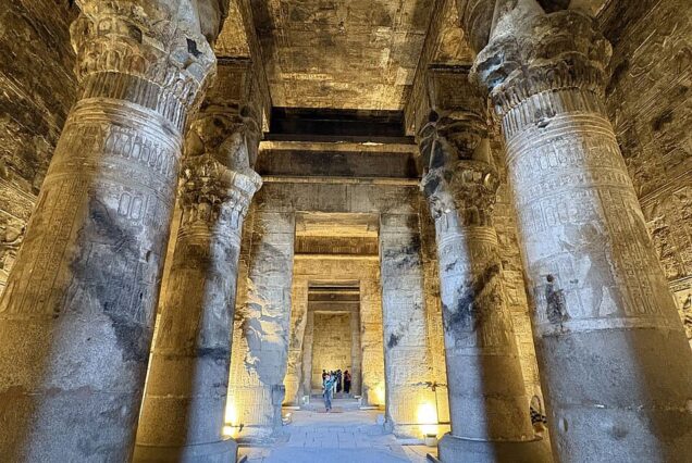 Interior of the Great Hypostyle Hall at the Temple of Hathor in Dendera, Egypt, showing eighteen Hathor-headed columns and detailed ceiling engravings.