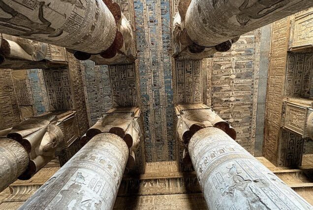 Interior of the Great Hypostyle Hall at the Temple of Hathor in Dendera, Egypt, showing eighteen Hathor-headed columns and detailed ceiling engravings.