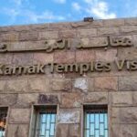 Sign for the Karnak Temples Visitor Center in Luxor, Egypt, displayed on a stone building with English and Arabic text.