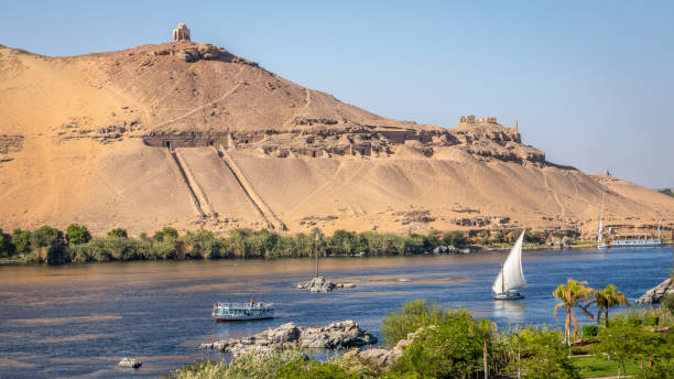 Rock-cut tombs of Qubbet el-Hawa on the west bank of the Nile in Aswan, Egypt, overlooking the river and desert cliffs.