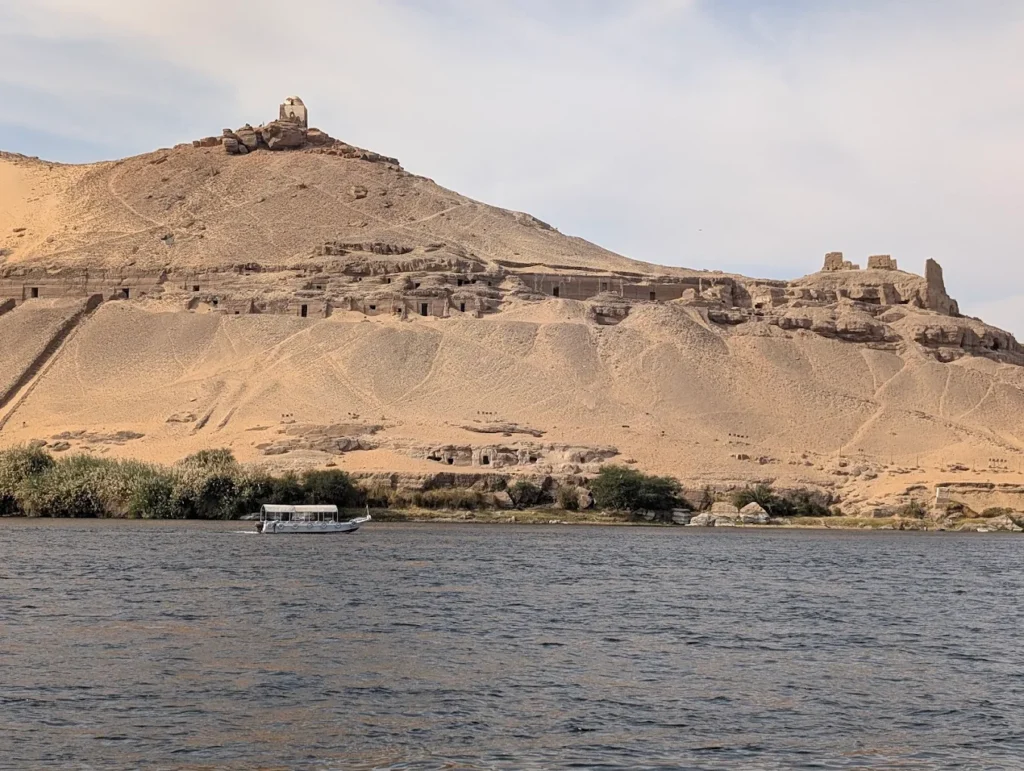 Qubbet el-Hawa archaeological site in Aswan, Egypt, showing rock-cut tombs of ancient nobles on the cliffs above the Nile River.