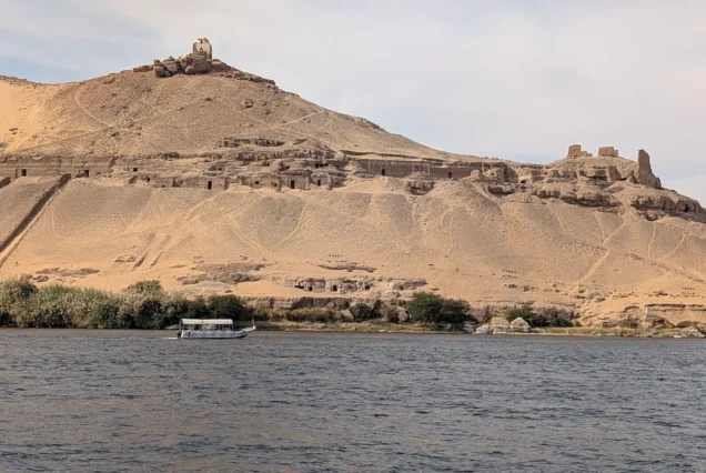 Qubbet el-Hawa archaeological site in Aswan, Egypt, showing rock-cut tombs of ancient nobles on the cliffs above the Nile River.