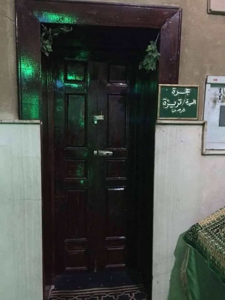"Wooden door with a green Arabic sign reading 'Jar of Lady Teresa, may God be pleased with her,' part of a shrine linked to a Christian woman who lived in Luxor’s early Islamic period."and embraced Islam.
