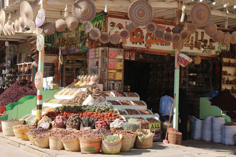 "Colorful market stall in Aswan Souk displaying spices, herbs, woven baskets, and handicrafts."